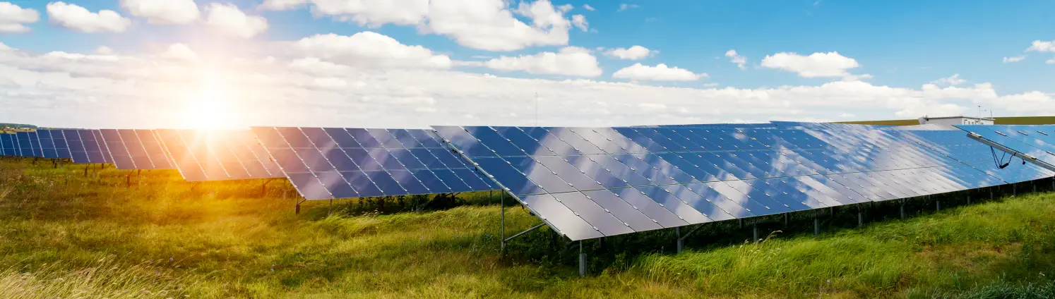 Solarpark in Brandenburg bei Sonnenaufgang. Weiße Wolken spiegeln sich in den Solarmodulen.