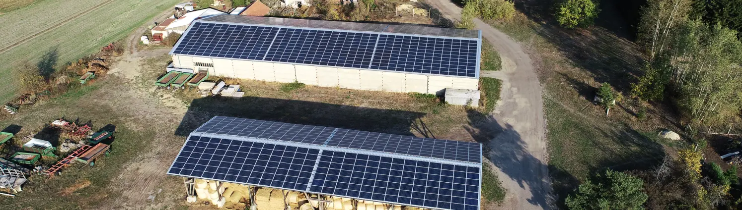 Photovoltaik-Dachanlage: Zwei langgestreckte Gebäude einer Agrargenossenschaft in Kahsel mit dunklen Solarmodulen auf dem Dach.