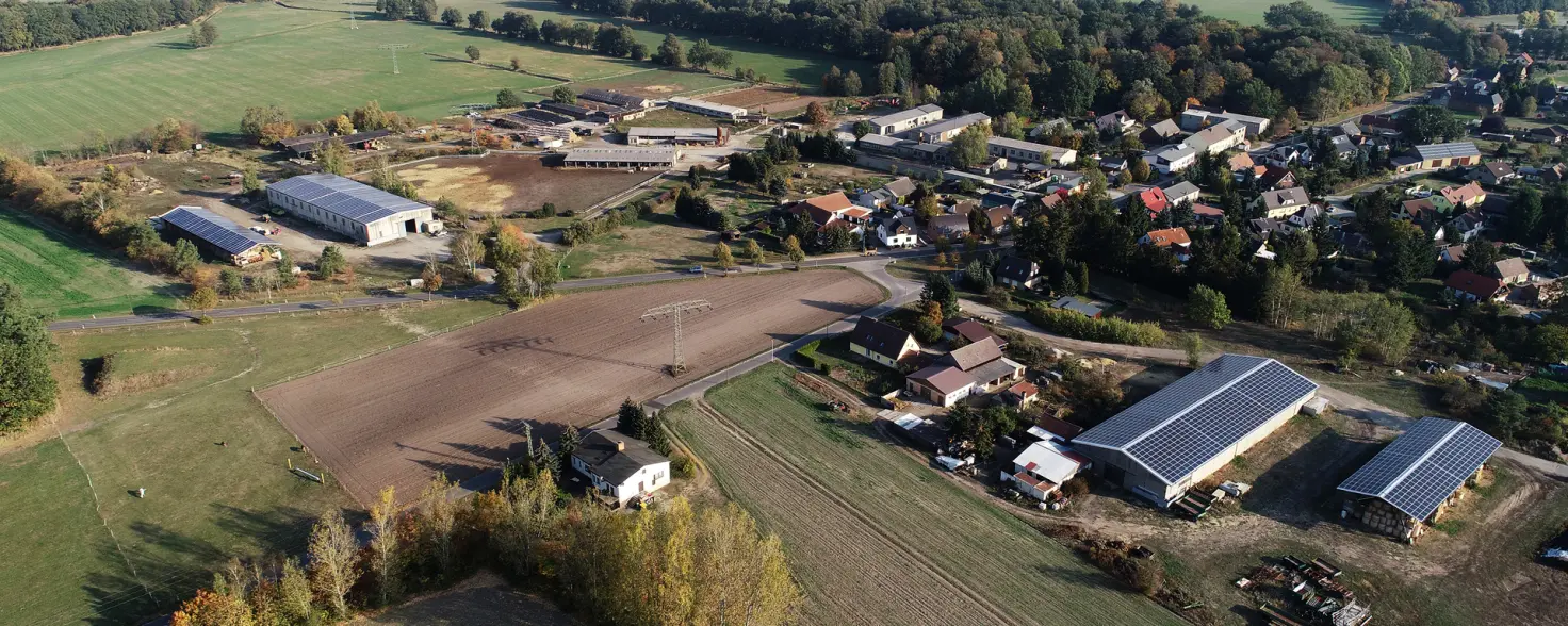 PV-Dachanlage: Wirtschaftsgebäude der Agrargenossenschaft Kahsel mit Solarmodulen auf dem Dach. Dahinter der Ort, Felder und Wälder.