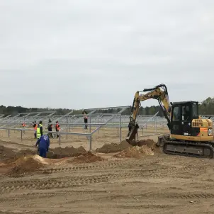 Baustelle des Solarparks Frauendorf: Ein Bagger und mehrere Arbeitende in Schutzkleidung installieren die Modulgestelle für die Solarpanels.
