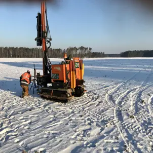 Schweres Gerät: Rotorange Ramme auf der Baustelle des Solarparks Frauendorf in der Lausitz. Die Fläche ist verschneit. Drumherum sind Wälder.